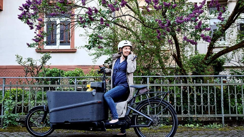 Eine JobRadlerin auf dem Lastenrad blickt zurück auf ihr Handy Eine JobRadlerin auf dem Lastenrad blickt zurück auf ihr Handy