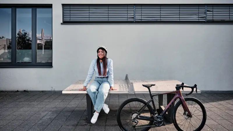 Eine Frau sitzt auf einer Tischtennisplatte, ihr Gravelbike steht neben ihr Eine Frau sitzt auf einer Tischtennisplatte, ihr Gravelbike steht neben ihr