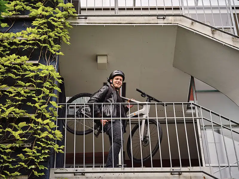 JobRadler trägt Fahrrad die Treppe herunter und lacht in Kamera JobRadler trägt Fahrrad die Treppe herunter und lacht in Kamera