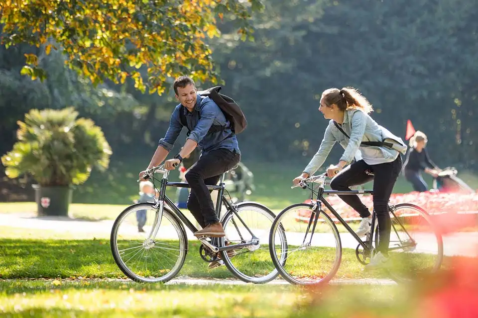 Zwei Radfahrer:innen fahren im Herbst durch den Park, Seitenansicht Zwei Radfahrer:innen fahren im Herbst durch den Park, Seitenansicht