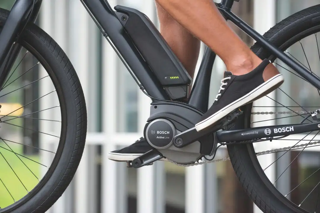Foto mit Zoom auf den Bosch-Motor eines E-Bikes, auf dem Pedal Füße in Canvasschuhen Foto mit Zoom auf den Bosch-Motor eines E-Bikes, auf dem Pedal Füße in Canvasschuhen